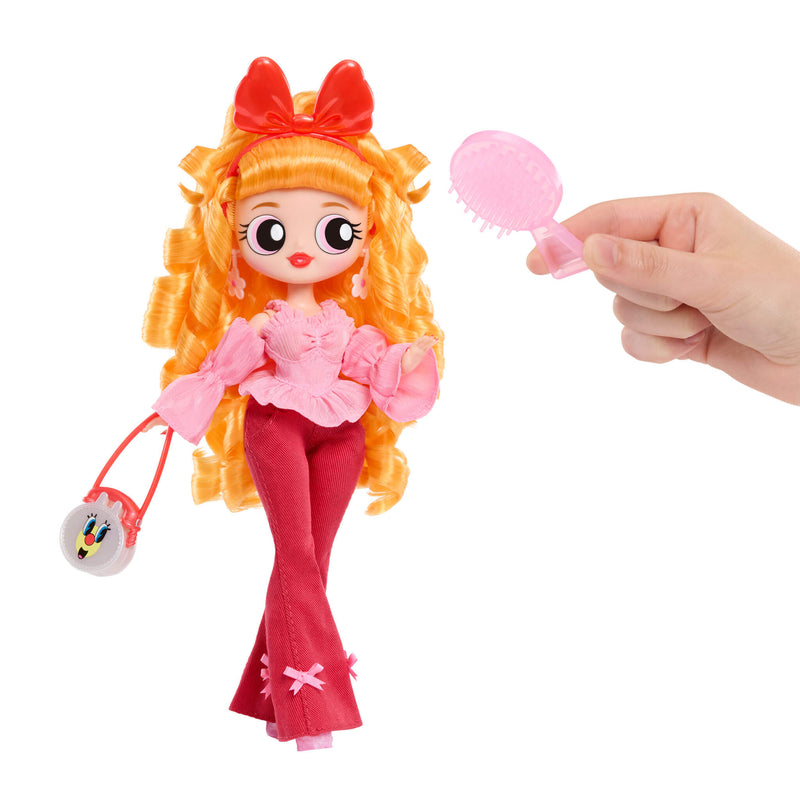 Toy doll with orange hair and pink outfit holding a brush, with a hand holding a brush near it on a white background.