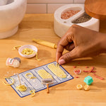 Hand interacting with miniature pasta-making tools on a wooden surface