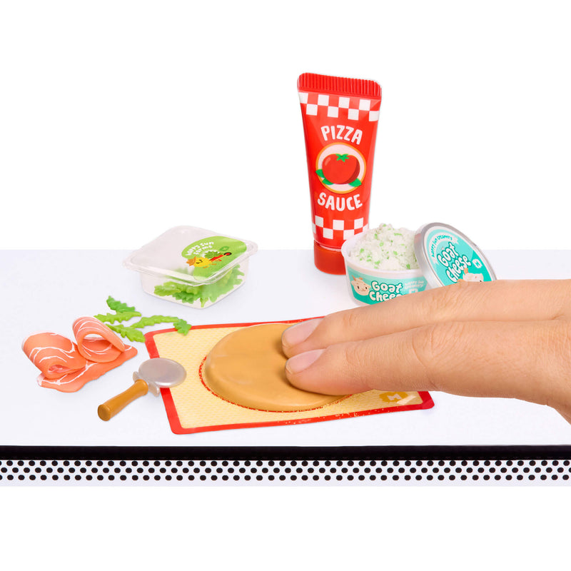 Playset with mini pizza ingredients and a hand interacting with them on a white background.