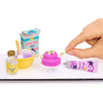 Miniature baking set with a hand adding decoration to a pink cake.