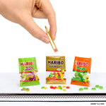 Haribo candy packages with a hand holding a gold tweezers on a white background