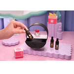 Hand holding a dropper over a black round container on a pink and purple surface with cosmetic items.