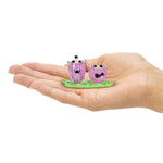 Two mini purple drinks with black eyes on a green base held in a hand 