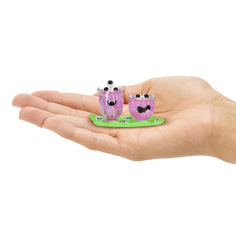 Two mini purple drinks with black eyes on a green base held in a hand 