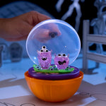 Toy with purple characters inside a clear ball on an orange base, held by a hand.