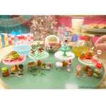 Miniature food and drink set on a green surface with festive background