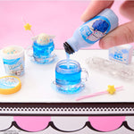 Blue liquid being poured from a bottle into small cups with a pink background