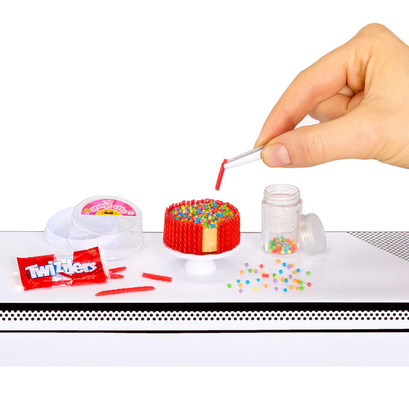 Hand decorating a small cake with colorful sprinkles on a white surface.