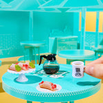 Miniature coffee set on a small table with a hand holding a mug.