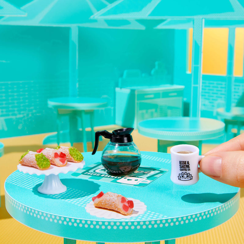 Miniature coffee set on a small table with a hand holding a mug.