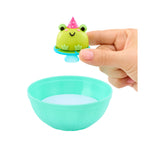 Small green frog toy with a pink party hat on top of a teal bowl held by a hand.