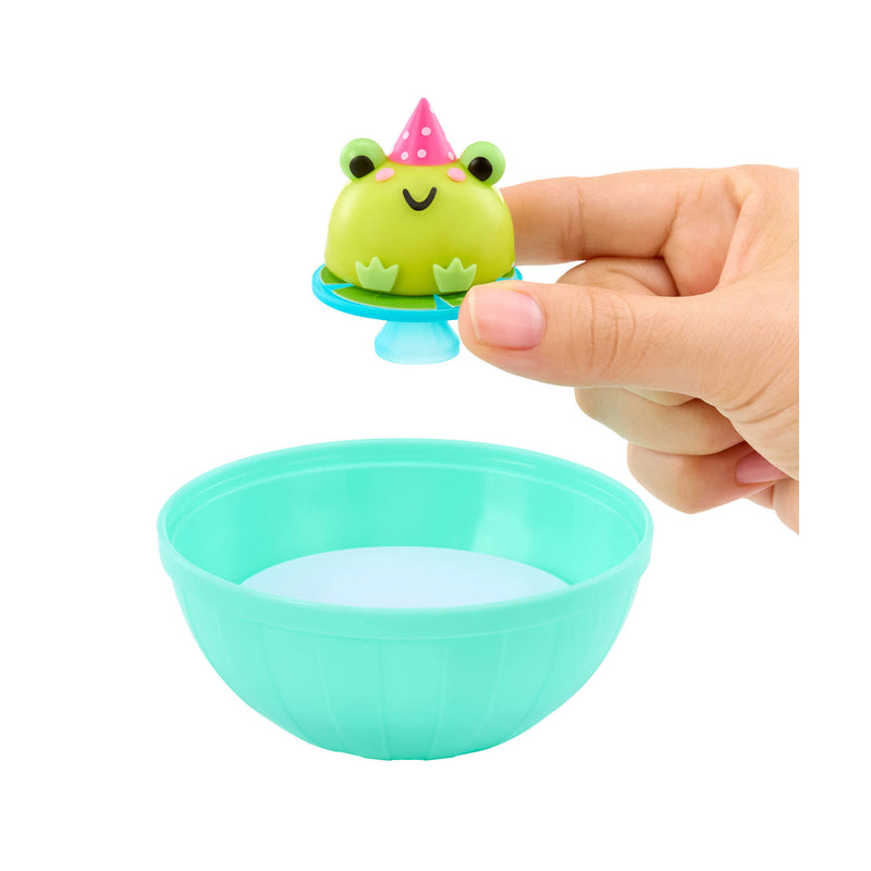 Small green frog toy with a pink party hat on top of a teal bowl held by a hand.
