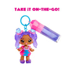 Small doll with purple hair and a pink outfit holding a colorful bottle, with 'Take It On-The-Go!' text above.