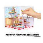 Miniature model of a kitchen scene with a hand adding a gold object, set against a white background.
