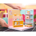 Miniature ice cream shop set with 'Happy Sun Creamery' branding, held by a hand on a tiled floor.