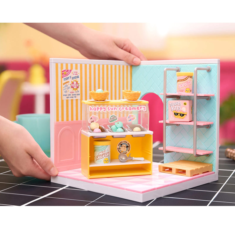 Miniature ice cream shop set with 'Happy Sun Creamery' branding, held by a hand on a tiled floor.