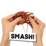 Hands holding two cake pops with a 'SMASH!' card in front on a white background