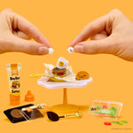 Miniature food set with hands interacting on a yellow background