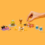 Miniature food models on a yellow background with a hand interacting with them.