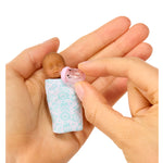 Mini baby in a blue blanket held on palm of hand on a white background