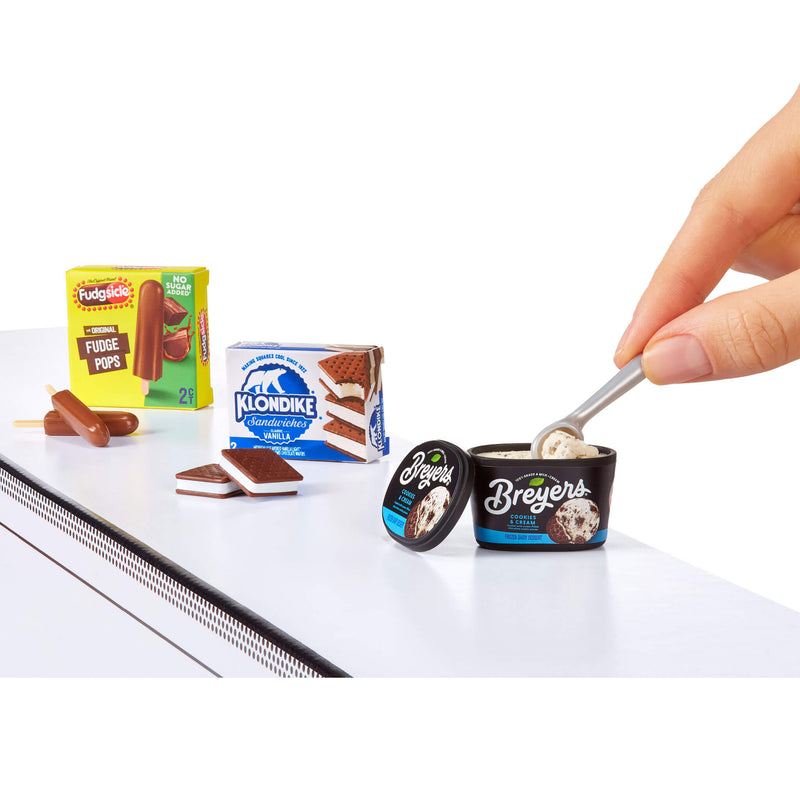 Miniature ice cream containers and packaging on a white surface with a hand using a spoon.