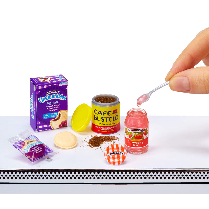 Miniature food items including a box of Unibestables, a jar of Cafe Bustelo coffee, a jar of Skucker's strawberry jelly, and a packet of cookies on a white surface.
