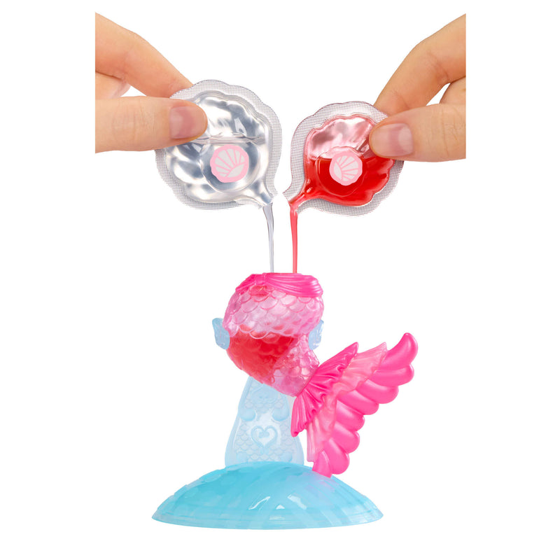 Toy figure of a mermaid with pink tail and blue holder being filled with a red  and a clear liquid from small pouches.