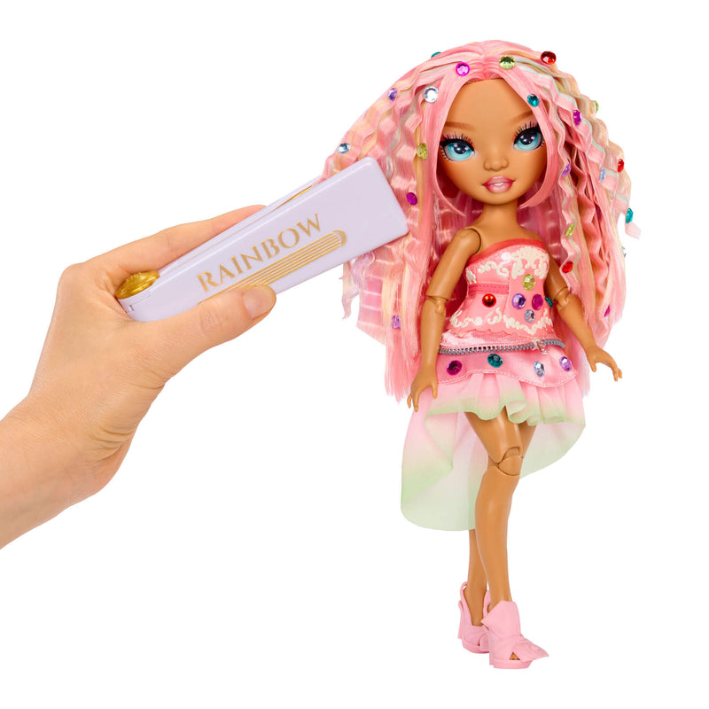 Hand holding a toy bedazzling tool with 'Rainbow' branding next to a doll with pink hair and outfit.