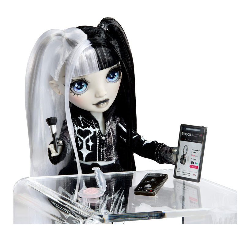 Doll with black hair and white ponytail, sitting at a table with electronic devices.