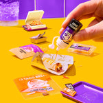 Person adding sauce to a Taco Bell burrito on a yellow table with various Taco Bell products.