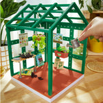 Toy greenhouse with gardening accessories on a wooden floor