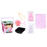 Collection of items including a Tataba box, pink pom-poms, a black dish, and a pink floral-patterned paper on a white background.