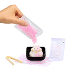 Hand pouring pink powder into a small black container with a plush toy inside, on a white background.