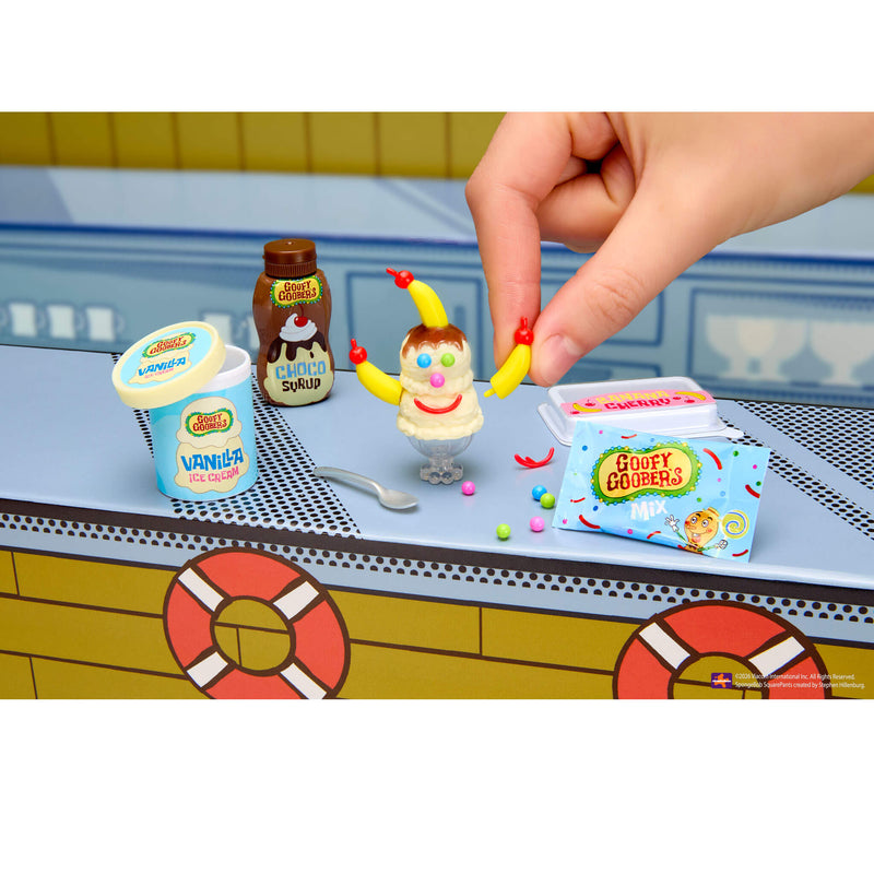 Toy set with a character and various items on a table, with a hand interacting with the toys.