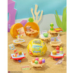Toy set with a yellow ball labeled 'Make It Mini' surrounded by miniature food items and accessories on a sandy background.