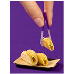 Hand holding a purple taco holder with a taco, with more tacos on a black plate below on a purple background