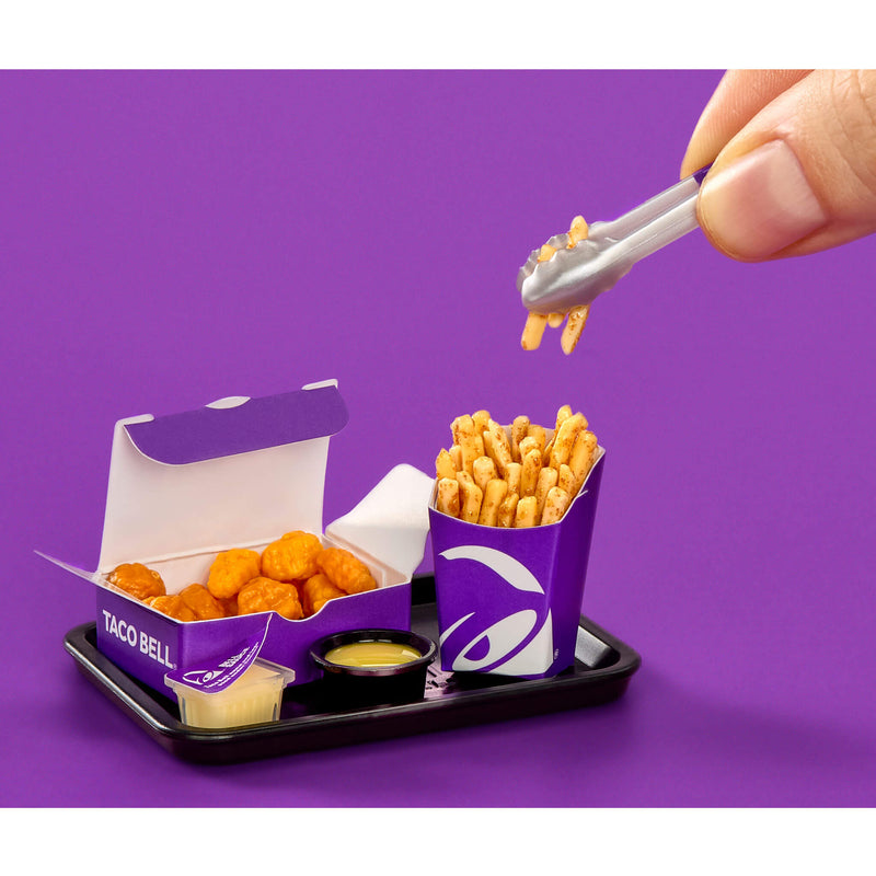 Taco Bell food items on a tray with a hand using tongs on a purple background