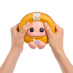 Toy resembling Hostess Cupcake with a face held between two hands on a white background