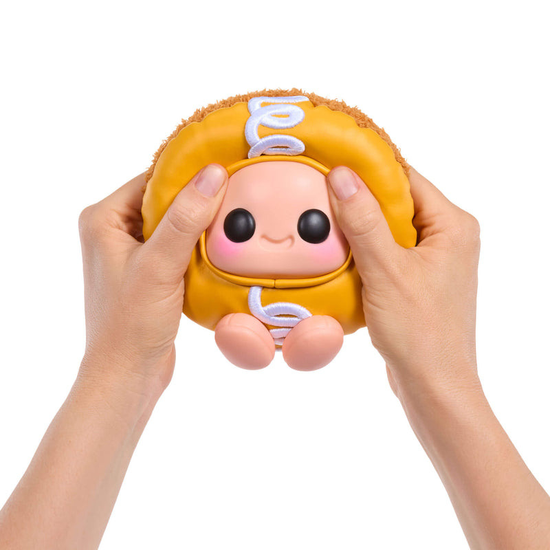 Toy resembling Hostess Cupcake with a face held between two hands on a white background