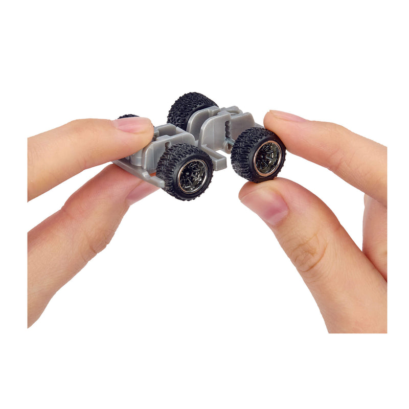 Close-up of hands holding a small truck base component with black wheels on a white background