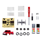 RC truck body kit and accessories laid out on a white background, including a red truck chassis, decals, clear plastic pieces, a red-handled screwdriver, spray cans, black rubber rings, and small hardware.
