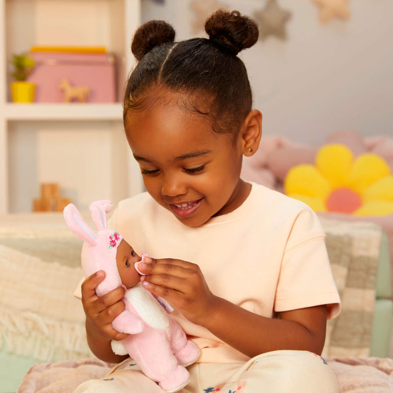 Young girl playing with a pink plush bunny doll in a cozy room.