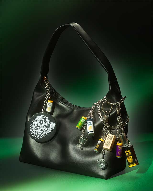 Black handbag with various Miniverse Liquid Death charms on a dark background