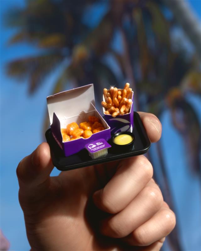 Hand holding a small purple box with  Minverse chicken nuggets and nacho fries against a blurred natural background