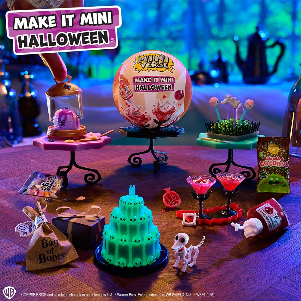 A tabletop display of a Halloween-themed miniature toy set under UV light, featuring a green skull-topped cake on a stand, a pink ball labeled 'Make It Mini Halloween,' small candy stands with decorative items, cocktail glasses, a skull figure, and packaging accessories. The scene is styled with spooky props and a purple glow.