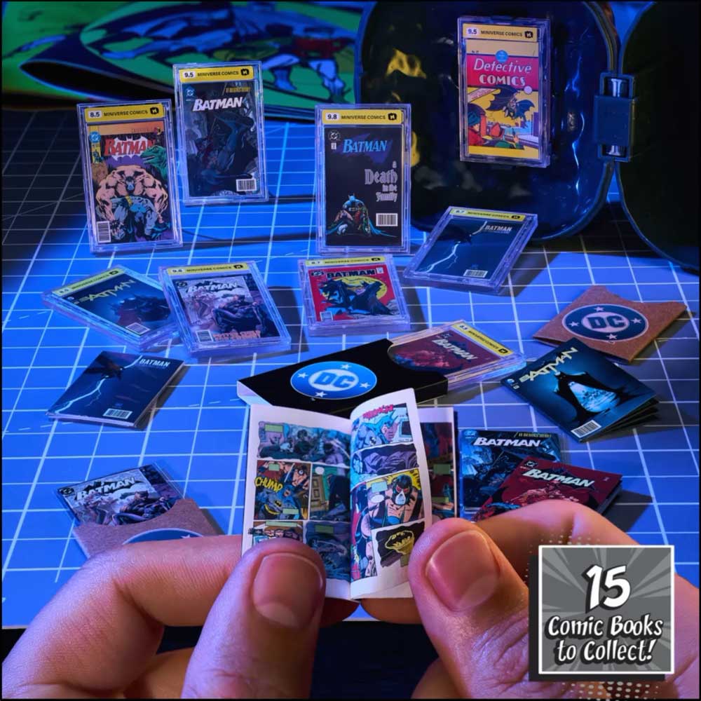 A person's hands hold an open miniature comic book set, surrounded by many small comic book cards and book covers arranged on a blue grid surface. The scene includes Batman and Detective Comics items, with a badge in the corner reading '15 Comic Books to Collect!'.